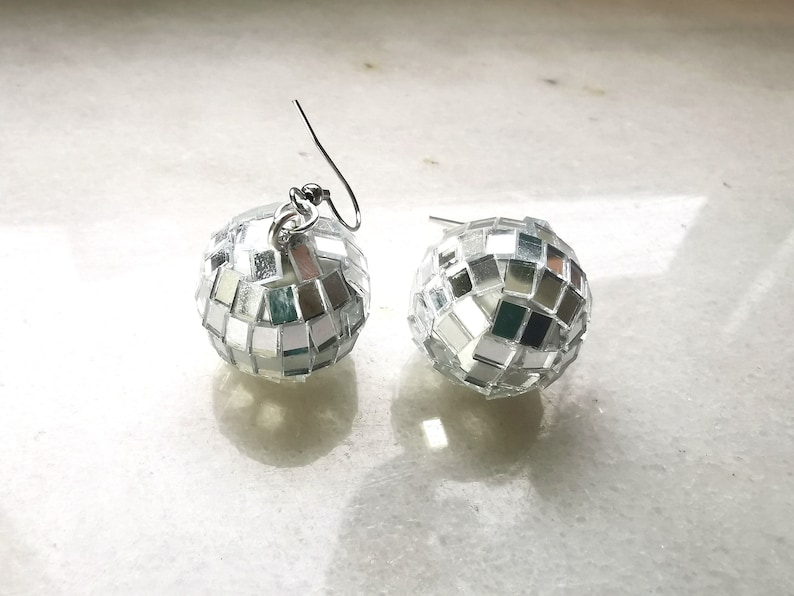 May include: A pair of silver disco ball earrings. Each earring is a small sphere covered in mirrored tiles.