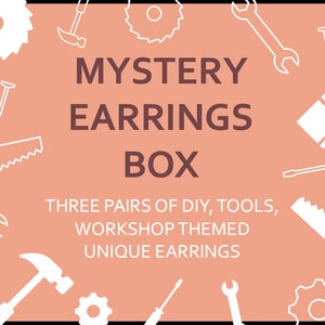 Op de afbeelding: Een roze achtergrond met witte contouren van gereedschap, waaronder een zaag, een hamer, een sleutel, een schroevendraaier, een kwast en spijkers. De tekst "MYSTERY EARRINGS BOX" is in bruin. Onder de tekst staat "THREE PAIRS OF DIY, TOOLS, WORKSHOP THEMED UNIQUE EARRINGS."