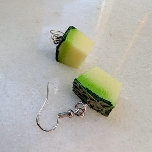 Peut inclure: Une paire de boucles d'oreilles en forme de tranches de pastèque vertes et blanches. Les boucles d'oreilles sont en pâte polymère et ont des crochets argentés.