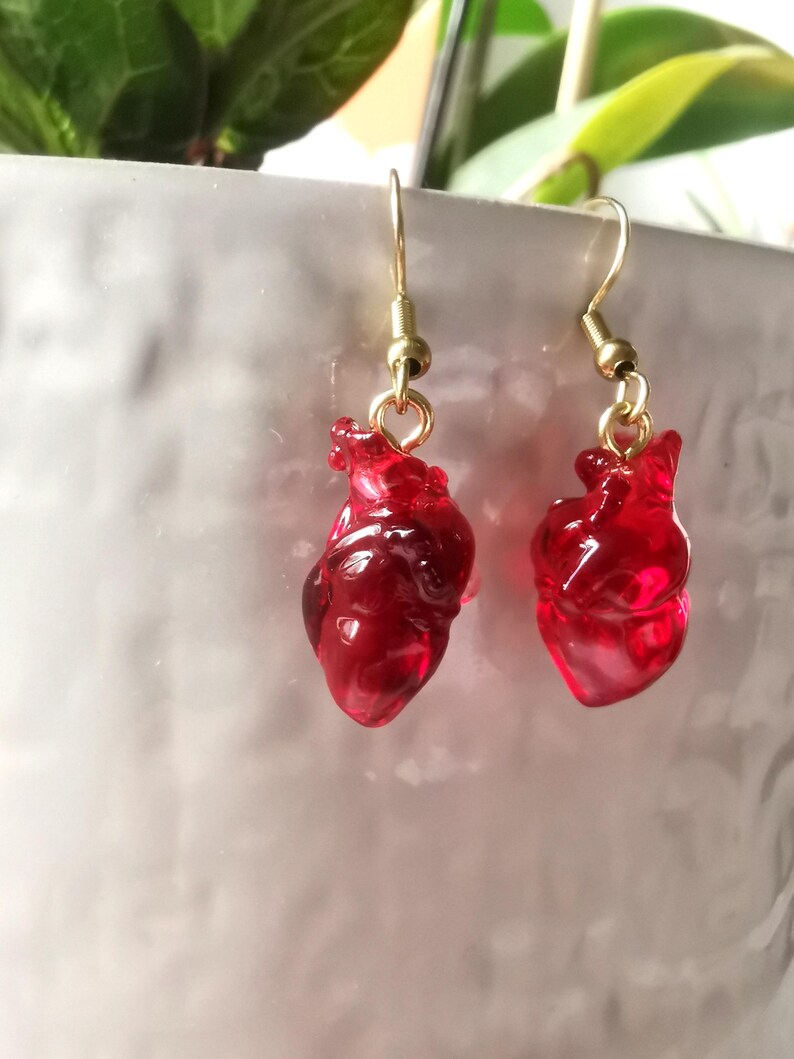 May include: A pair of gold earrings with red glass heart charms. The hearts are detailed and realistic.