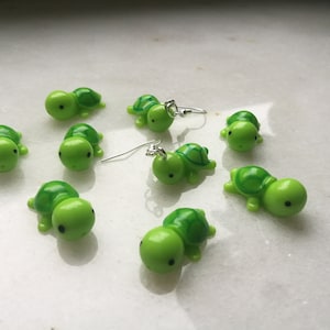 Op de afbeelding: Negen groene schildpad oorbellen met zilveren haakjes. De schildpadden hebben zwarte ogen en een groene schild met een donkergroene omtrek.