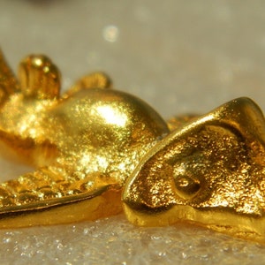 Puede incluir: Un colgante de color dorado con forma de pájaro estilizado con las alas extendidas. El colgante tiene un diseño detallado y un acabado liso y brillante.