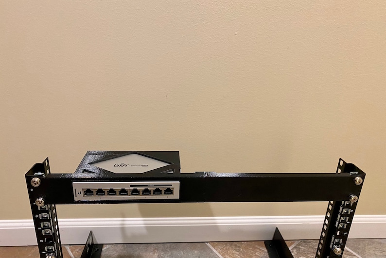 May include: A black metal server rack with a silver 8-port network switch mounted on the top. The switch has the text "Ubiquiti" printed on it.