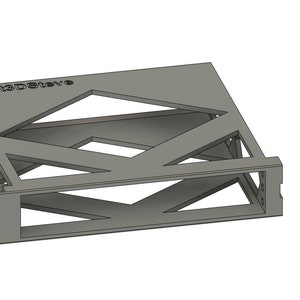 May include: A grey 3D printed stand with a geometric design. The stand has a rectangular base and a raised platform with an open design. The text "PRINTED BY" is visible on the top of the stand.
