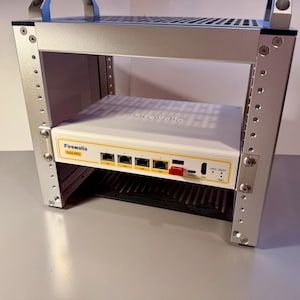 May include: A silver metal rack with a white and yellow Firewalla device installed. The device has multiple ports and a red button. The rack has handles on top and is designed to hold electronic equipment.