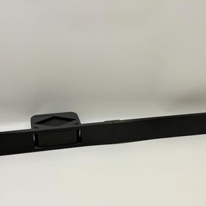 May include: A black, rectangular rack mount component with a handle and mounting holes. The component has a central section with a recessed handle and a raised section with a diamond-shaped design.