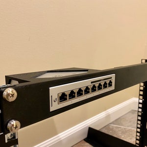 May include: A black metal rack with a silver network switch mounted on it. The switch has eight ports labeled 1 through 8.