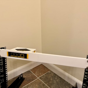 Può includere: Un rack in metallo bianco con una struttura in metallo nero. Il rack ha uno scaffale bianco con un dispositivo nero montato su di esso. Il dispositivo ha quattro porte gialle.