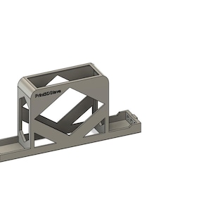 Puede incluir: Objeto plateado renderizado en 3D, con base rectangular y sección rectangular superior abierta. El diseño incluye cortes geométricos y el texto "Print3Dstore". El objeto parece ser un soporte o base.