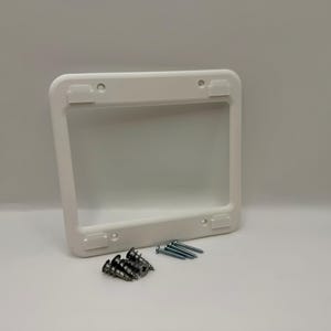 May include: A white rectangular electrical box cover with rounded corners. The cover has four mounting tabs and is accompanied by a set of screws. The cover is designed to protect and conceal electrical components.