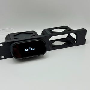 Puede incluir: Soporte de rack negro impreso en 3D con un dispositivo GL.iNet. El dispositivo tiene una pantalla negra con texto blanco. El soporte de rack tiene dos orificios de montaje y un diseño geométrico.