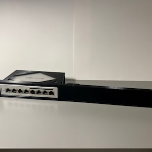 May include: A black metal rack with a silver 8-port ethernet switch mounted on it. The rack has two mounting holes on each side.