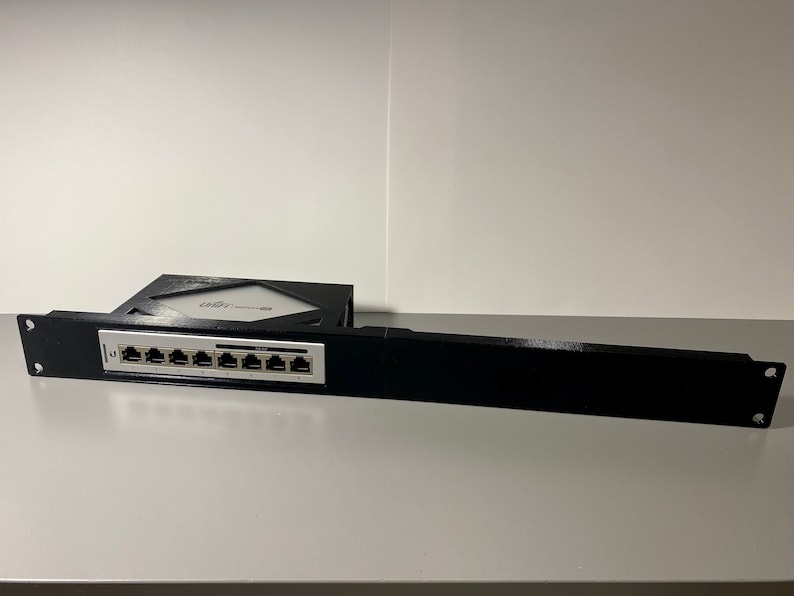 May include: A black metal rack with a silver 8-port ethernet switch mounted on it. The rack has two mounting holes on each side.