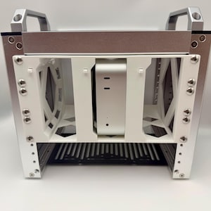 以下が含まれることがあります： 上部にハンドルが付いたシルバーと白のコンピューターケース。ケースは長方形で、内部は白、外部はシルバーです。ケースの前面には黒いグリルがあります。