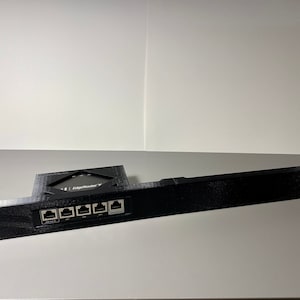 May include: Black 3D printed rack with a cutout for a router and five ethernet ports. The rack is labeled "EdgeRouter X".