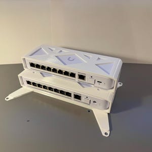 以下が含まれることがあります： 2つの白いネットワークスイッチが積み重ねられています。スイッチには複数のポートがあり、白いスタンドに接続されています。