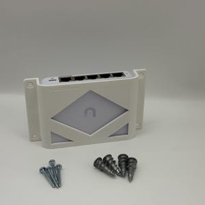 May include: A white network switch with a diamond-shaped design and the text "ProtectSmart". Includes a set of screws for mounting. The switch has multiple ports for network connections.