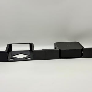 以下が含まれることがあります： 電子機器用の黒いラックマウント。マウントは長方形で、中央に開口部があり、正方形のデバイスを保持するセクションがあります。各端に取付穴があります。