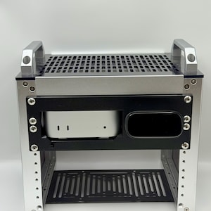 May include: A silver and black computer case with a perforated top and bottom shelf. The case has a rectangular black frame that holds a small white computer. Two silver handles are on top.