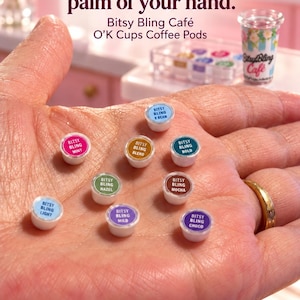 May include: Miniature coffee pods labeled Bitsy Bling Caf&eacute; O'K Cups. The pods feature various colors and text including V Bean, Mint, Blend, Bold, Hazel, Mocha, Light, Mild, and Choco. The text reads: So much caf&eacute; in the palm of your hand.