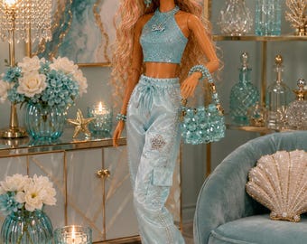 Könnte beinhalten: Eine Modepuppe mit langem, welligem blondem Haar und rosa Strähnen, bekleidet mit einem hellblauen, glitzernden Neckholder-Top mit 'Bitsy'-Anhänger, passender hellblauer Satin-Cargohose mit Sternaufnäher und hellblauen Riemchen-High-Heels.