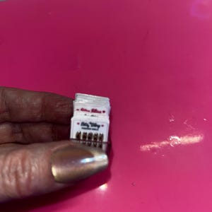 May include: A small stack of white rectangular cards featuring the text Bitty Bling and a row of five tiny metallic studs at the bottom. Each card is identical, displaying the brand name in a dark font with small red heart icons on either side.