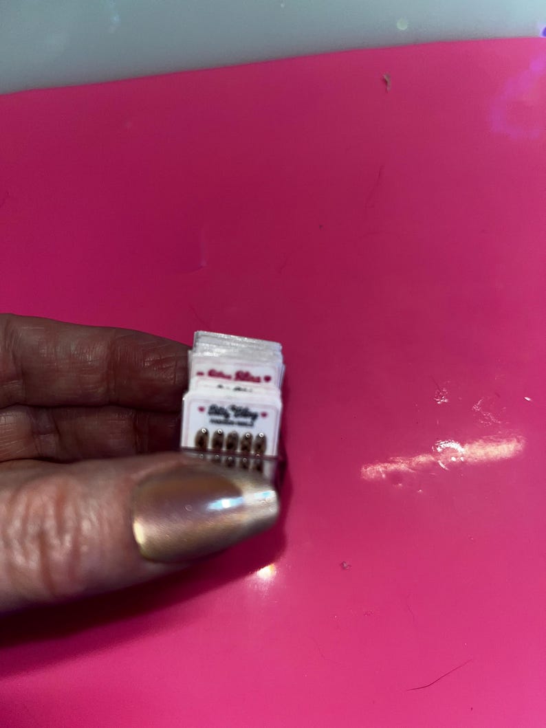 May include: A small stack of white rectangular cards featuring the text Bitty Bling and a row of five tiny metallic studs at the bottom. Each card is identical, displaying the brand name in a dark font with small red heart icons on either side.