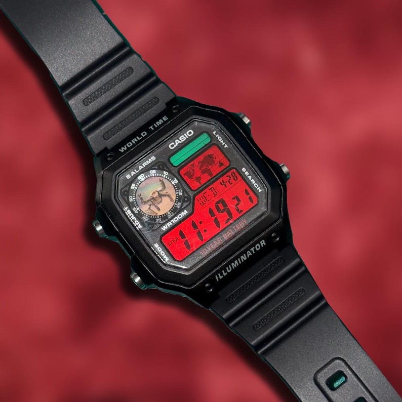 Puede incluir: Reloj digital Casio negro con una pantalla digital roja que muestra la hora y la fecha. El reloj tiene una correa negra y una esfera cuadrada con el texto "CASIO", "WR100M" e "ILLUMINATOR". La hora mostrada es 11:19:21.