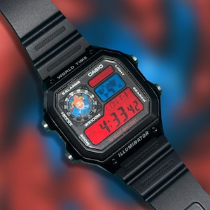 May include: Black Casio digital watch with a red digital display showing the time 4:33:42 PM. The watch face has a colorful design with a cartoon character. Features include world time, alarms, and a 10-year battery.