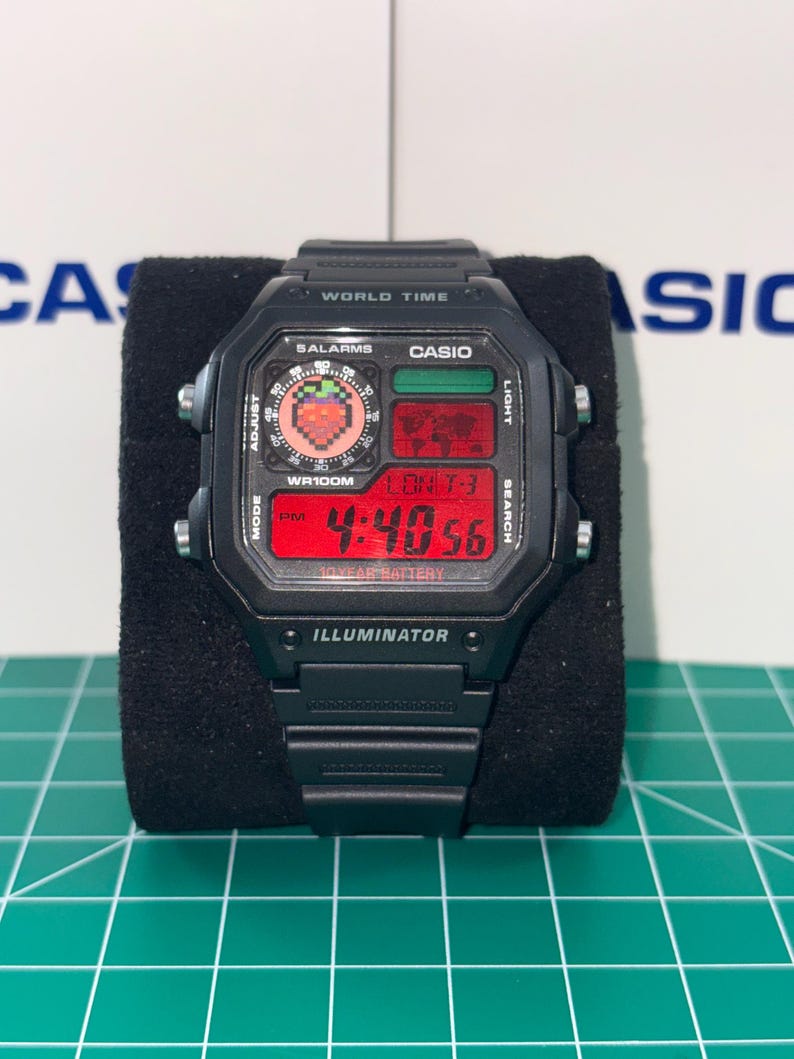 May include: Black digital watch with a rectangular face. The watch displays the time in red digits and features the text "WORLD TIME", "SALARMS", "CASIO", and "ILLUMINATOR". The watch has a black band and buttons.