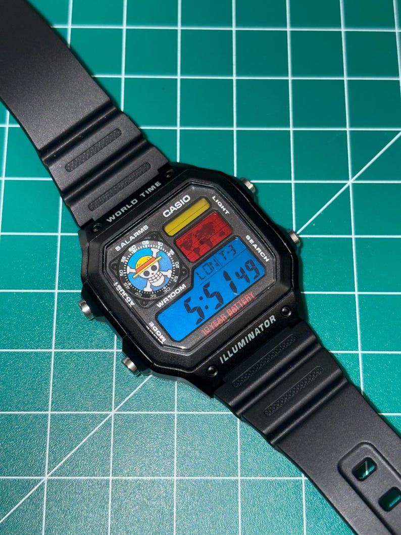 K&ouml;nnte beinhalten: Schwarze digitale Casio-Uhr mit rechteckigem Zifferblatt. Die Uhr zeigt die Uhrzeit, das Datum und andere Funktionen auf einem blauen Digitalbildschirm an. Das Zifferblatt der Uhr tr&auml;gt die Aufschrift "CASIO", "WR100M" und "ILLUMINATOR". Das Armband der Uhr ist schwarz.