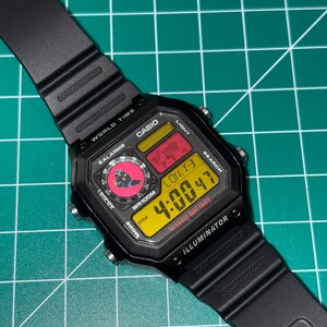 Peut inclure: Montre num&eacute;rique Casio noire avec un cadran rectangulaire. L'heure affich&eacute;e est 4:00:47 en chiffres jaunes. La montre a un bracelet noir et affiche le texte "ILLUMINATOR" et "10 YEAR BATTERY".