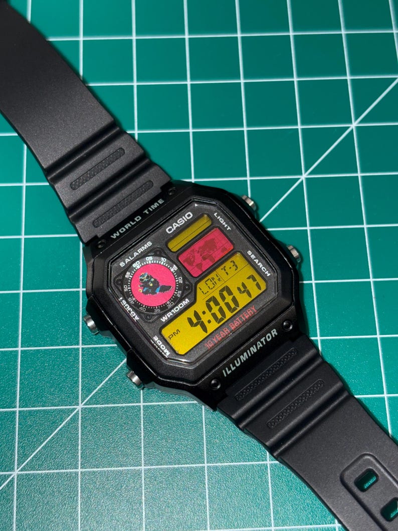Peut inclure: Montre num&eacute;rique Casio noire avec un cadran rectangulaire. L'heure affich&eacute;e est 4:00:47 en chiffres jaunes. La montre a un bracelet noir et affiche le texte "ILLUMINATOR" et "10 YEAR BATTERY".