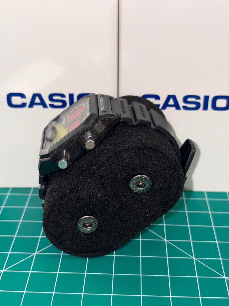 Peut inclure: Montre num&eacute;rique Casio noire avec un cadran rectangulaire et un bracelet noir. La montre est pr&eacute;sent&eacute;e sur un support en velours noir. Le mot "CASIO" est visible en arri&egrave;re-plan.