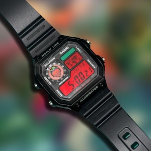 May include: Black Casio digital watch with a rectangular face and a black band. The watch face displays the time in red digits, along with other functions. The watch has the text "CASIO", "WORLD TIME", and "ILLUMINATOR".