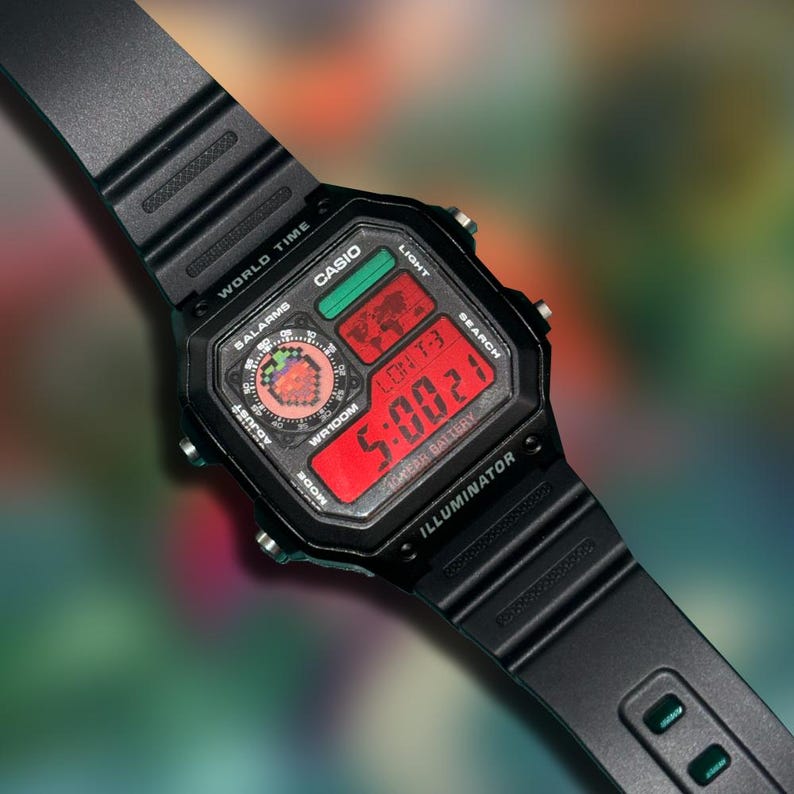 May include: Black Casio digital watch with a rectangular face and a black band. The watch face displays the time in red digits, along with other functions. The watch has the text "CASIO", "WORLD TIME", and "ILLUMINATOR".