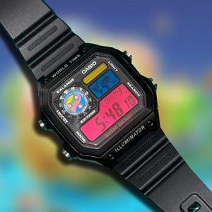 May include: Black Casio digital watch with a black band. The watch face displays the time in red digits, along with other functions. The watch has the text "CASIO", "WORLD TIME", and "ILLUMINATOR".