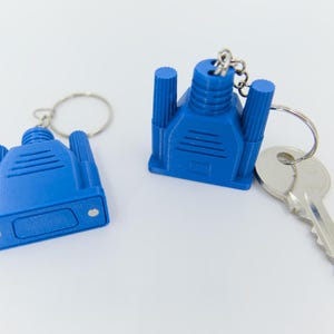May include: Two blue VGA connector keychains with silver key rings and a silver key. The keychains are a bright blue color and have a detailed design. The keychains are on a white background.