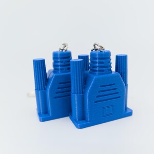 May include: Two blue VGA connectors with silver key rings. The connectors have a rectangular base with a series of parallel lines and cylindrical posts. The background is plain white.