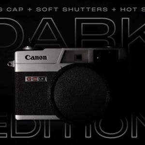 May include: A Canon G-III QL17 camera with a black lens cap. The camera has a silver top and a black textured body. The words "DARK EDITION" are displayed in a stylized font above and below the camera against a black background.