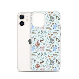 May include: A clear phone case with a light blue background and a pattern of baking-themed illustrations. The illustrations include a mixer, a pie, a cupcake, a cherry, a rolling pin, a spatula, and the words "yum!" and "baking".