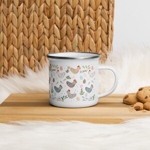 May include: White enamel mug with a pattern of colorful chickens, eggs, and flowers. The text "Cluck!" appears twice on the mug.