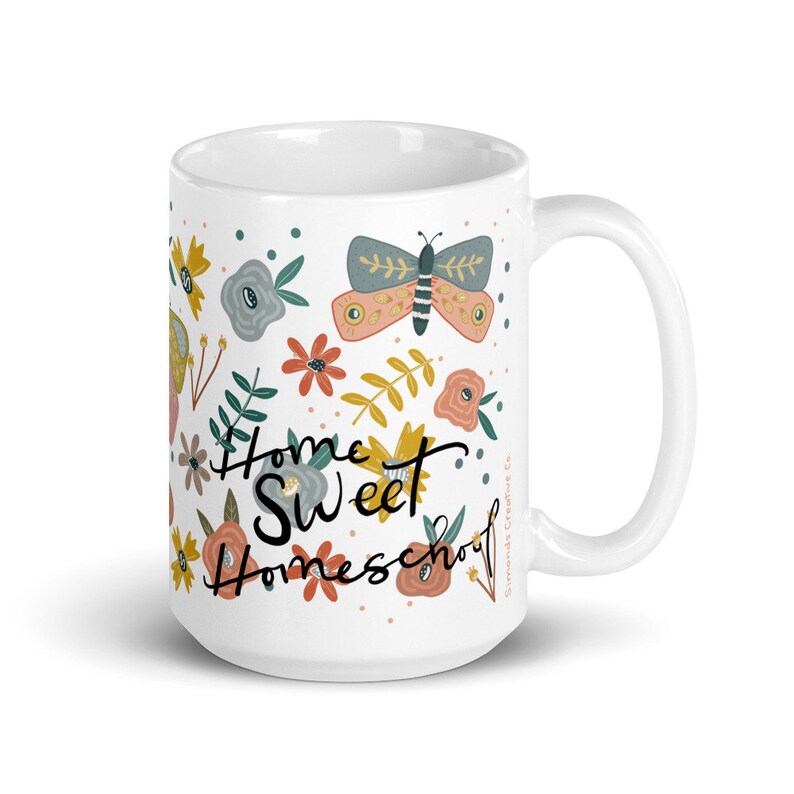 May include: White ceramic mug with a wraparound floral design featuring a butterfly, flowers, and the words "Home Sweet Homeschool" in black script. The mug has a curved handle and is suitable for hot or cold beverages.