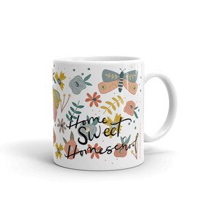 May include: White ceramic mug decorated with colorful floral and butterfly illustrations. The mug features the text "Home Sweet Homeschool" in a whimsical font, perfect for enjoying your favorite beverage.