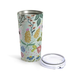 May include: A floral-patterned travel tumbler with a lid. The tumbler features a light green background with colorful flowers in pink, yellow, blue, and red. The lid is clear with a silver rim. The tumbler is designed to keep beverages hot or cold.