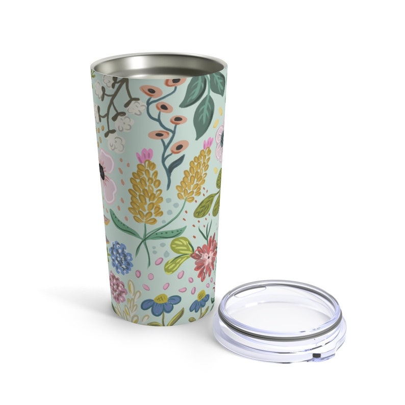 May include: A floral-patterned travel tumbler with a lid. The tumbler features a light green background with colorful flowers in pink, yellow, blue, and red. The lid is clear with a silver rim. The tumbler is designed to keep beverages hot or cold.