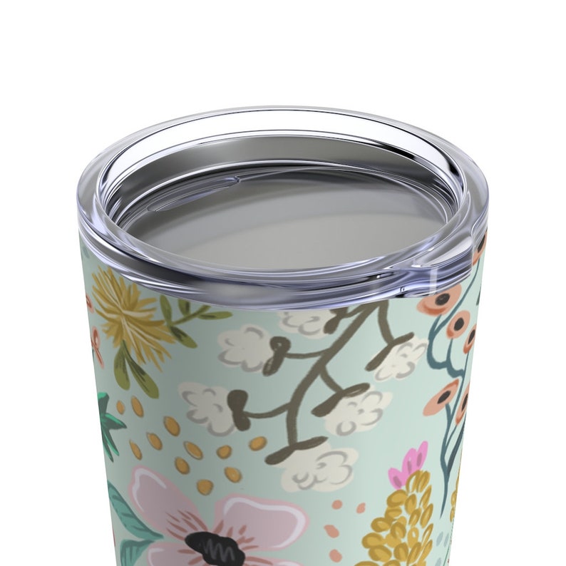 May include: A floral-patterned tumbler with a clear lid. The design features pink, yellow, and orange flowers with green leaves on a light blue background. The tumbler is designed to keep beverages hot or cold.