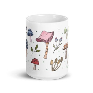 May include: White ceramic mug decorated with colorful illustrations of various mushrooms, leaves, and berries. The design features a whimsical, hand-drawn style with a pink, red, blue, and brown color palette. The mug is a standard size for coffee or tea.