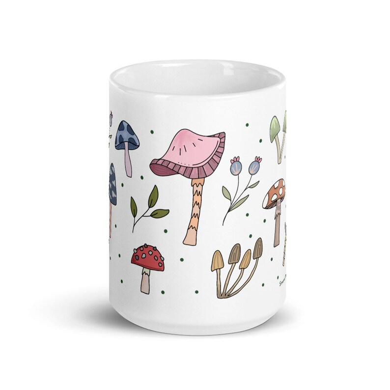 May include: White ceramic mug decorated with colorful illustrations of various mushrooms, leaves, and berries. The design features a whimsical, hand-drawn style with a pink, red, blue, and brown color palette. The mug is a standard size for coffee or tea.
