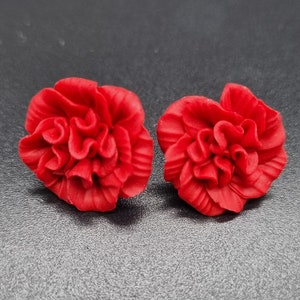 Könnte beinhalten: Ein Paar rote, blumenförmige Ohrringe. Die Ohrringe sind aus einem weichen, biegsamen Material gefertigt und haben eine zarte, gekräuselte Textur.